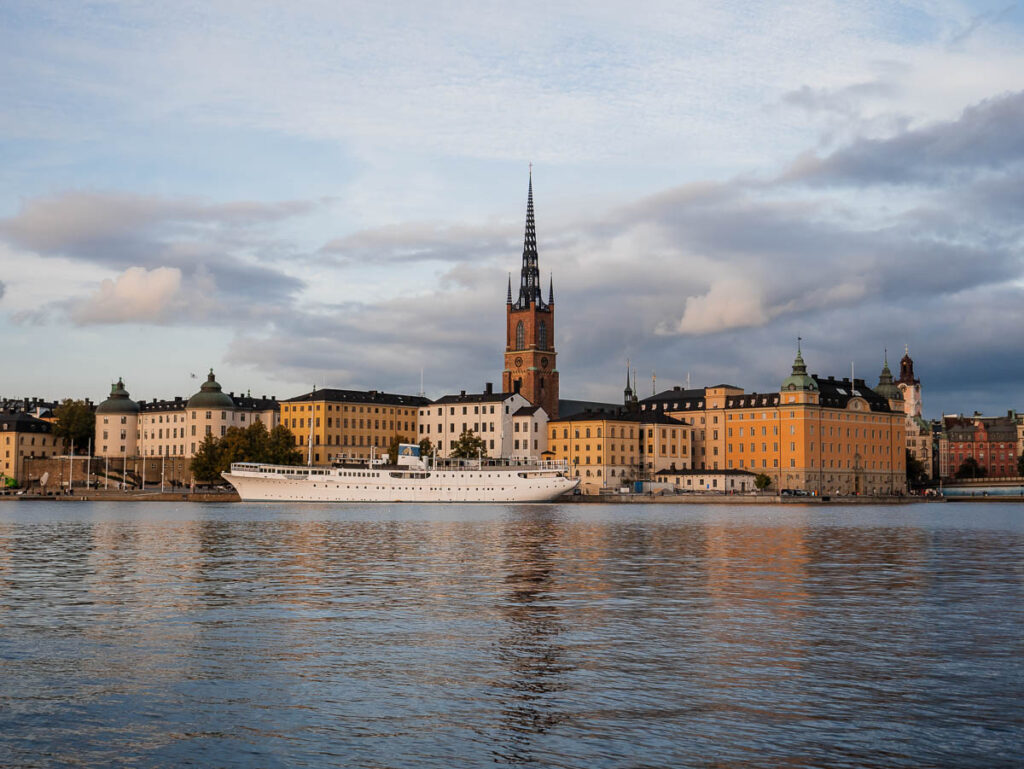 Panoramic view of Stockholm's waterfront with the iconic Riddarholmen Church spire rising above historic buildings, reflecting a serene evening sky. A must-visit if you're exploring Scandinavia by train