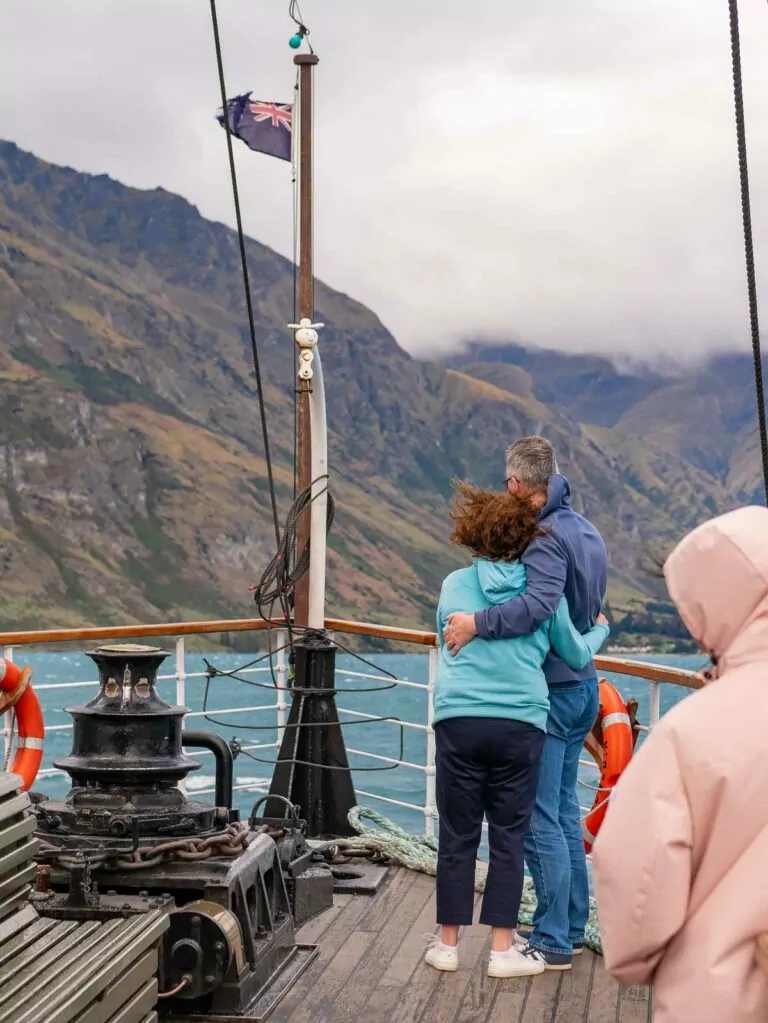Passengers on the deck of the TSS Earnslaw steamship, with a couple embracing and looking out at the mountainous landscape around Lake Wakatipu, New Zealand