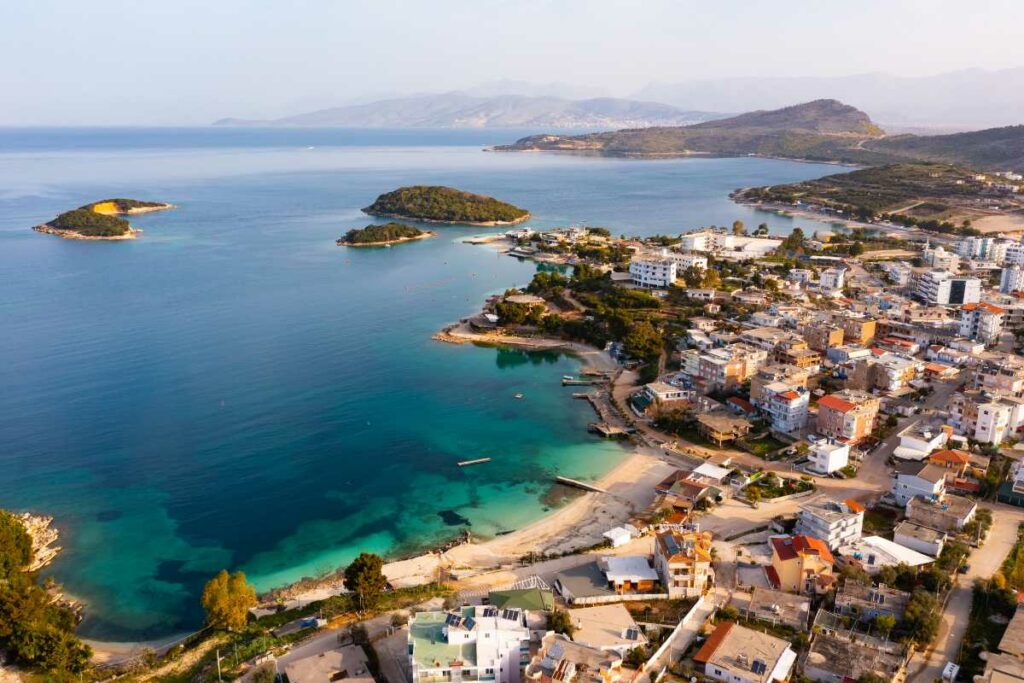 Aerial view of a coastal town on the Albanian Riviera with crystal-clear turquoise waters and surrounding greenery, ideal for a 2 week Balkans itinerary
