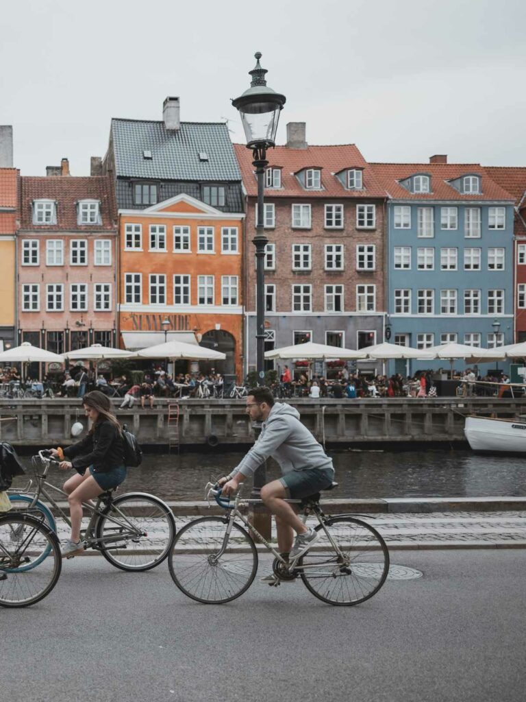 Cyclists crossing a bridge with the iconic colourful buildings of Nyhavn in the background, highlighting things to do alone in Copenhagen like enjoying a leisurely bike ride along the historic canals