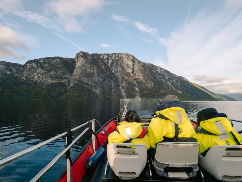 Tourists in bright yellow jackets enjoy a fjord safari in Flåm, Norway, with steep cliffs rising on either side of the calm waters, a memorable excursion in a 4 day Norway itinerary
