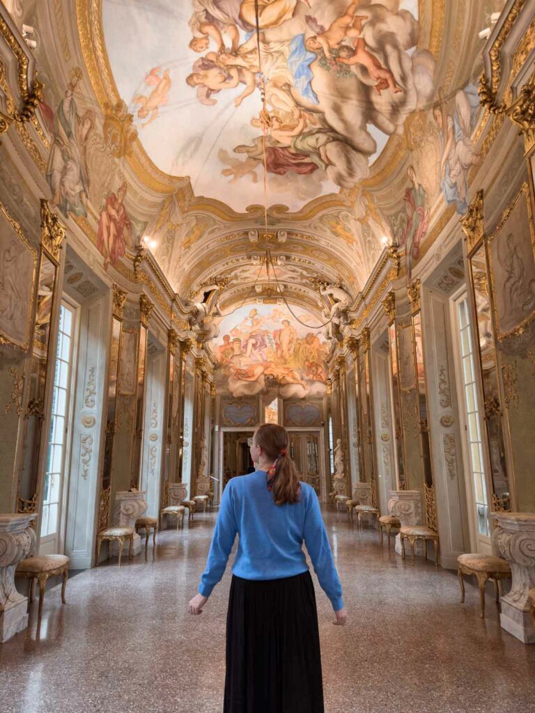 A visitor admiring the opulent baroque interior of the Royal Palace of Genoa, with intricate frescoes and luxurious decor, a highlight on a Northern Italy Switzerland itinerary