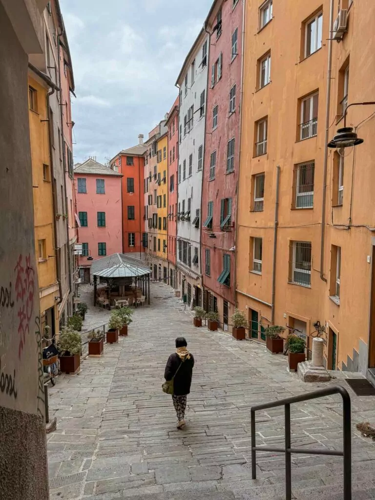 A person walking through a quaint alley lined with vibrant, multicolored buildings in Genoa, a must visit for a Northern Italy and Switzerland itinerary