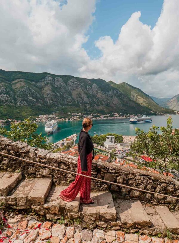 A person in a black top and red skirt stands on ancient stone steps overlooking the Bay of Kotor, Montenegro, a picturesque stop for any Balkans tour itinerary