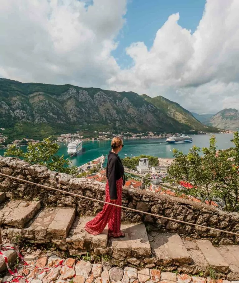 A person in a black top and red skirt stands on ancient stone steps overlooking the Bay of Kotor, Montenegro, a picturesque stop for any Balkans tour itinerary