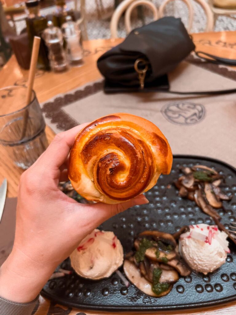 Hand holding a freshly baked pogacha bread above a plate of truffle cheese dip and mushrooms at Shtasteliveca