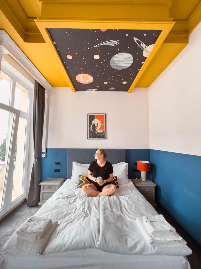 Woman reading on a bed in a space-themed room, ideal accommodation at INTROVERT Hotel for a whimsical 2 days in Sofia experience