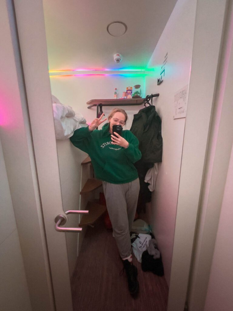 A mirror selfie of a visitor in a cosy, narrow hostel room, adorned with colourful LED lights, typical of a solo traveller's stay at CityHub hostel in Copenhagen