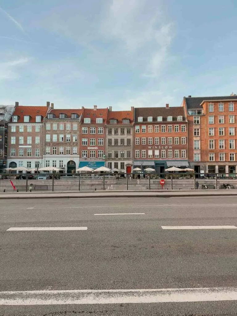 A clear day view across the street showcasing the row of vibrant, historical facades in Copenhagen, a perfect scene for travellers exploring the city's architecture while travelling to Copenhagen alone