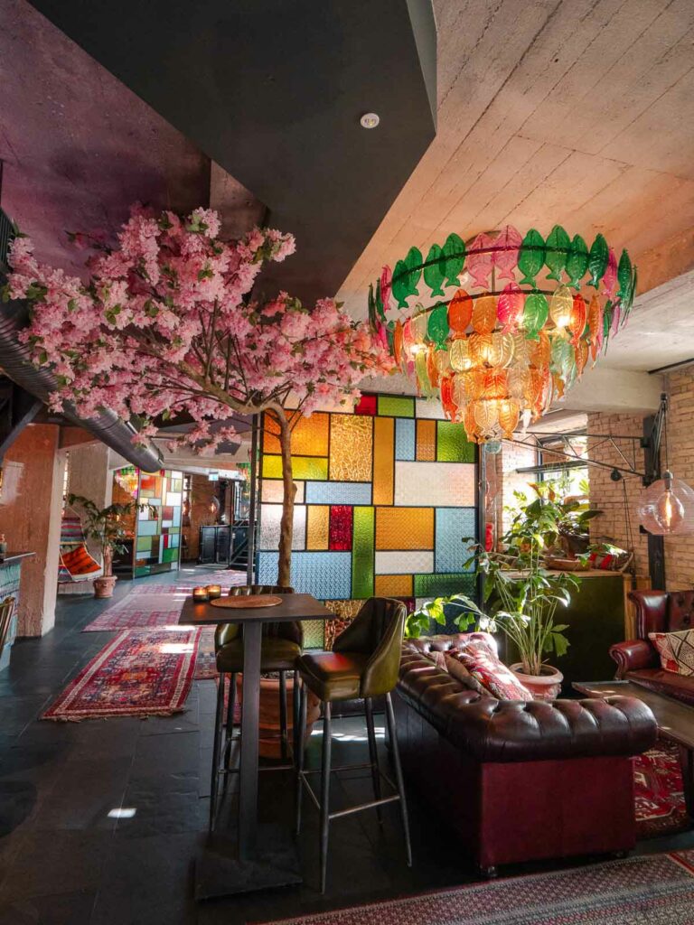 A bohemian-styled common area adorned with colourful lanterns and a ceiling of pink blossoms, embodying the quirky interior design at Bryggen Guldsmeden hotel in Copenhagen