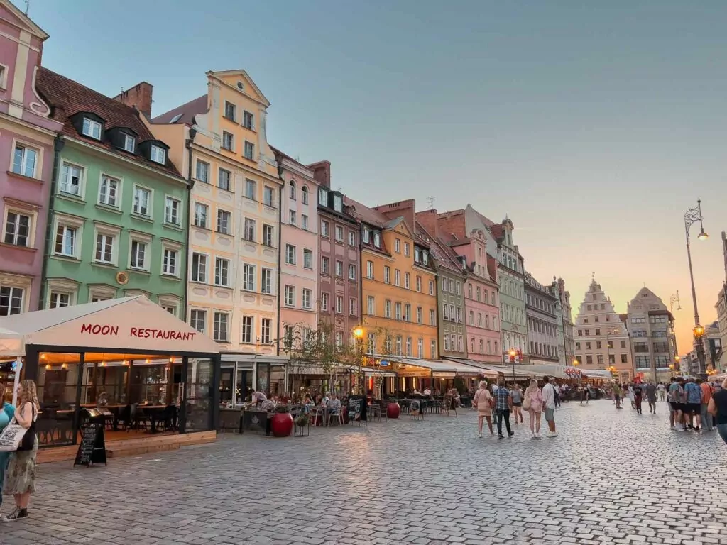 Charming pastel-coloured buildings line the streets of Wroclaw, Poland, with patrons enjoying the outdoor seating of the Moon Restaurant in the warm evening light