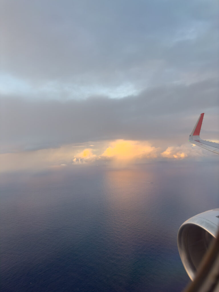 View from an airplane window featuring the wing and a beautiful sunset over the ocean, with the sky transitioning from light to dark, illustrating the start or end of an exciting journey