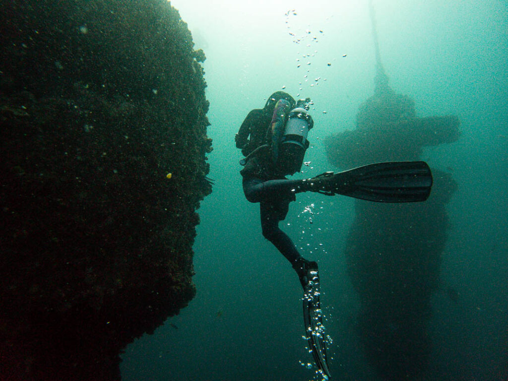 A scuba diver investigates an underwater artificial reef, surrounded by the deep blue ocean, creating an adventurous and mysterious diving experience