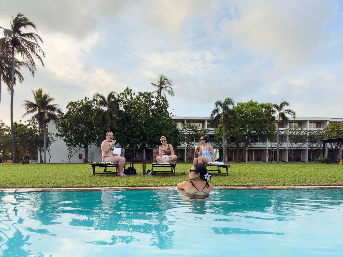 Three girls sitting on pool chairs overlooking the pool with one girl facing away from the camera in the water