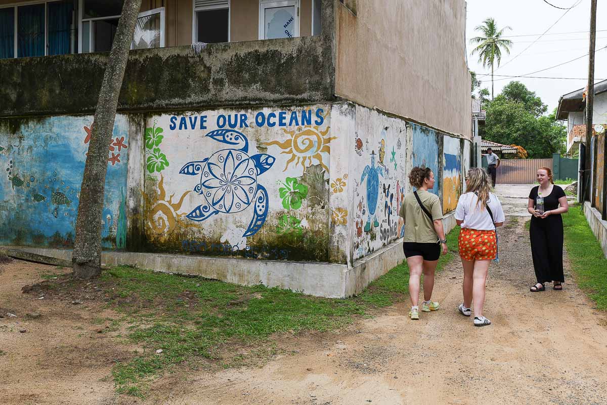 Travellers walking past a Save Our Oceans turtle mural in a coastal Sri Lankan village