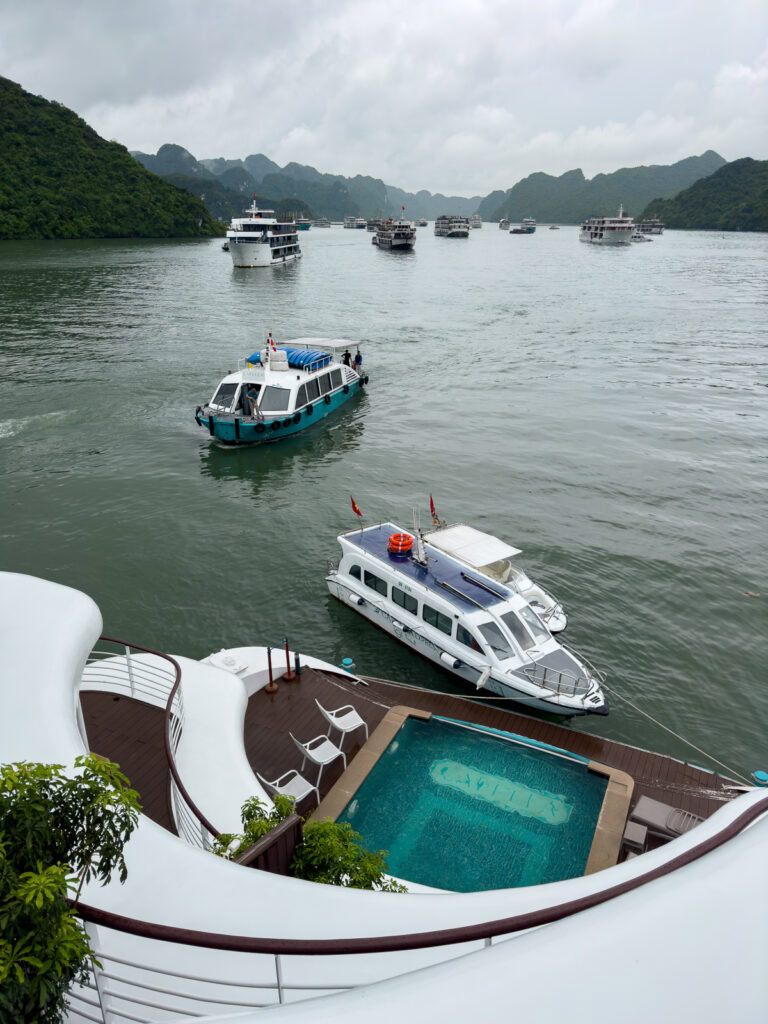 An overhead view of the Capella Cruise’s pool and surrounding deck, with boats navigating the calm waters of Halong Bay.