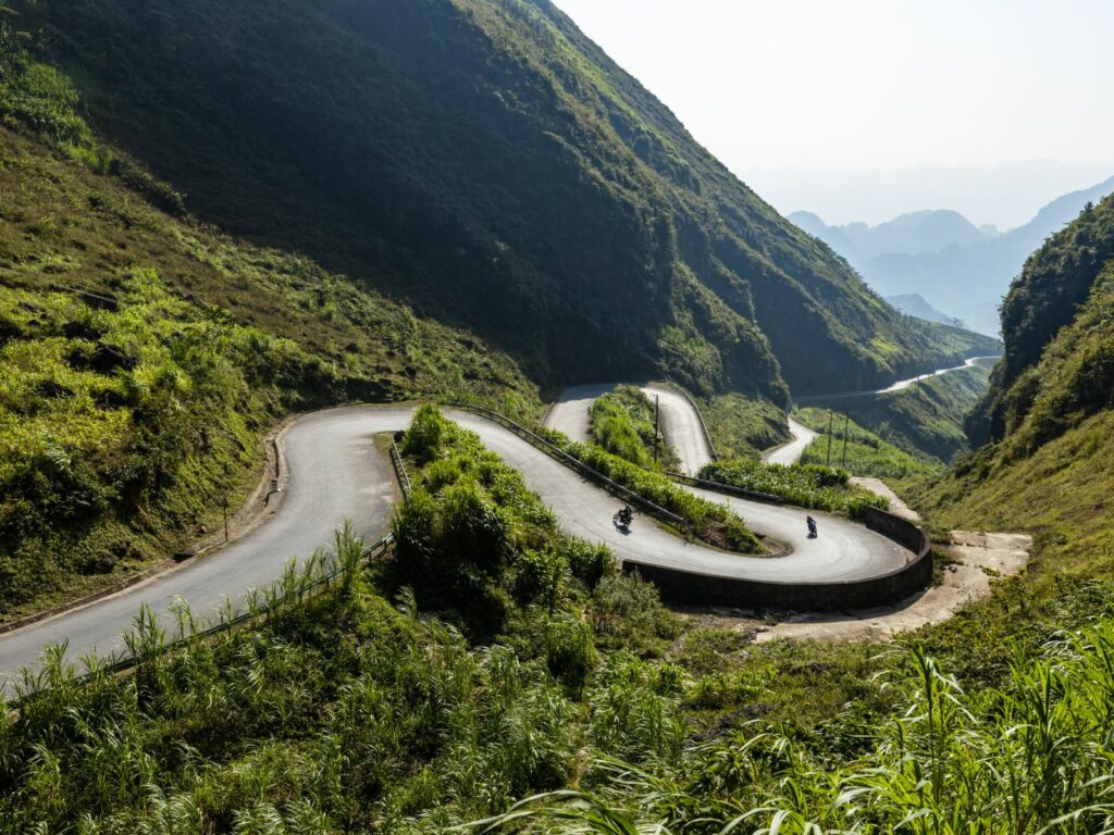 A winding mountain road with motorbikes making their way along steep, green hillsides in Ha Giang, Vietnam