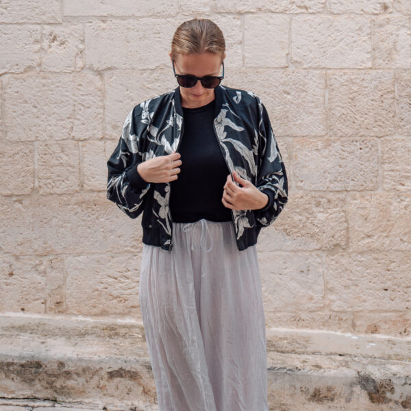 A woman in a stylish black and white floral bomber jacket and light-gray skirt adjusts her outfit, highlighting the unique fashion found at tailors in Hoi An