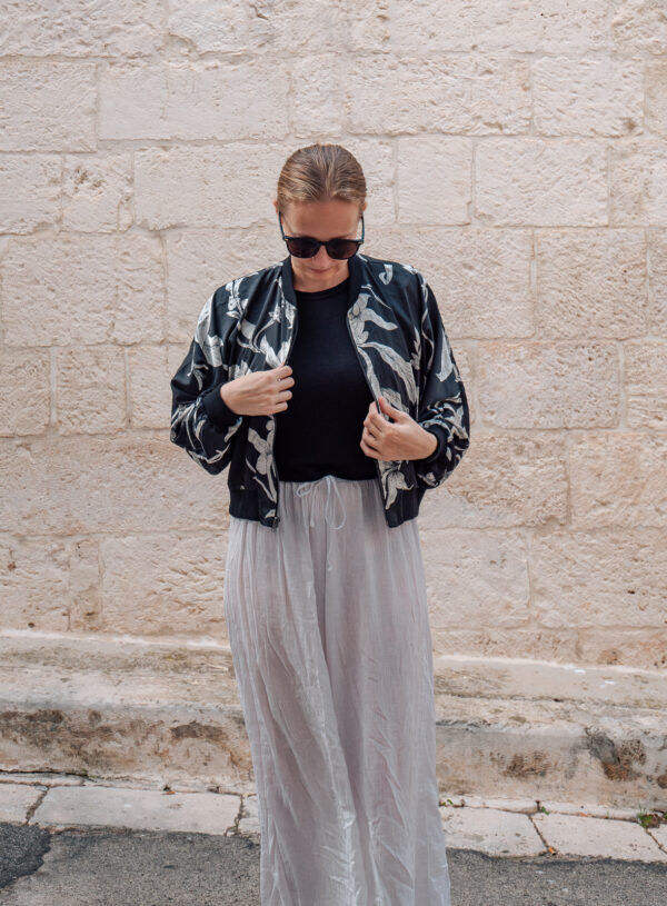 A woman in a stylish black and white floral bomber jacket and light-gray skirt adjusts her outfit, highlighting the unique fashion found at tailors in Hoi An