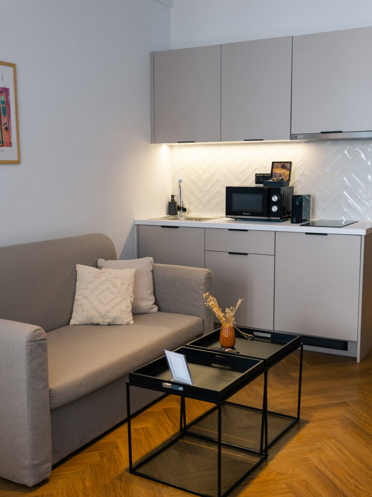 A cosy living area with a grey sofa, kitchenette, and coffee table, offering relaxation after a long week of exploring greek islands