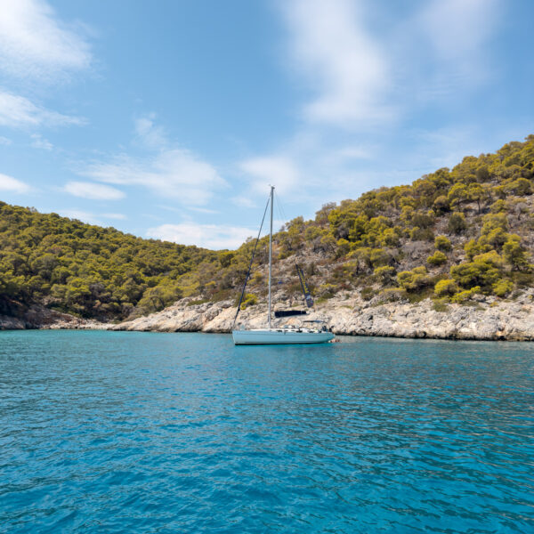 A sailboat anchored in a secluded bay with clear turquoise waters, epitomising a perfect greece yacht charter experience.