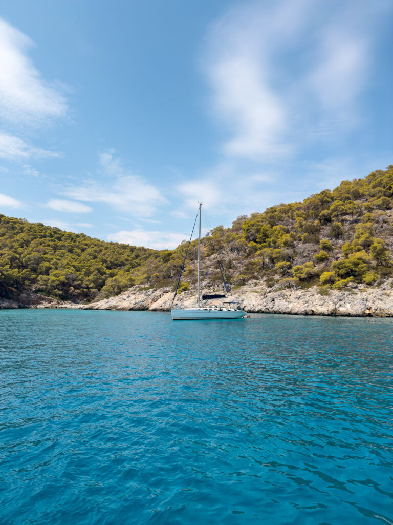 A sailboat anchored in a secluded bay with clear turquoise waters, epitomising a perfect greece yacht charter experience.
