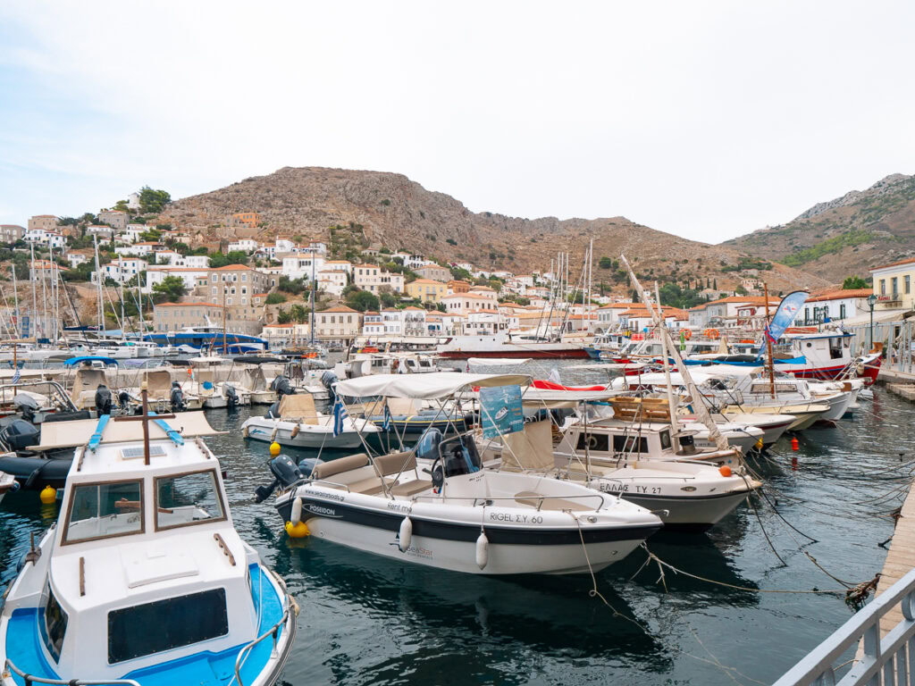 A bustling marina with a variety of boats tied up along the pier, surrounded by a charming town built into the hillside, a common sight during greek island hopping.