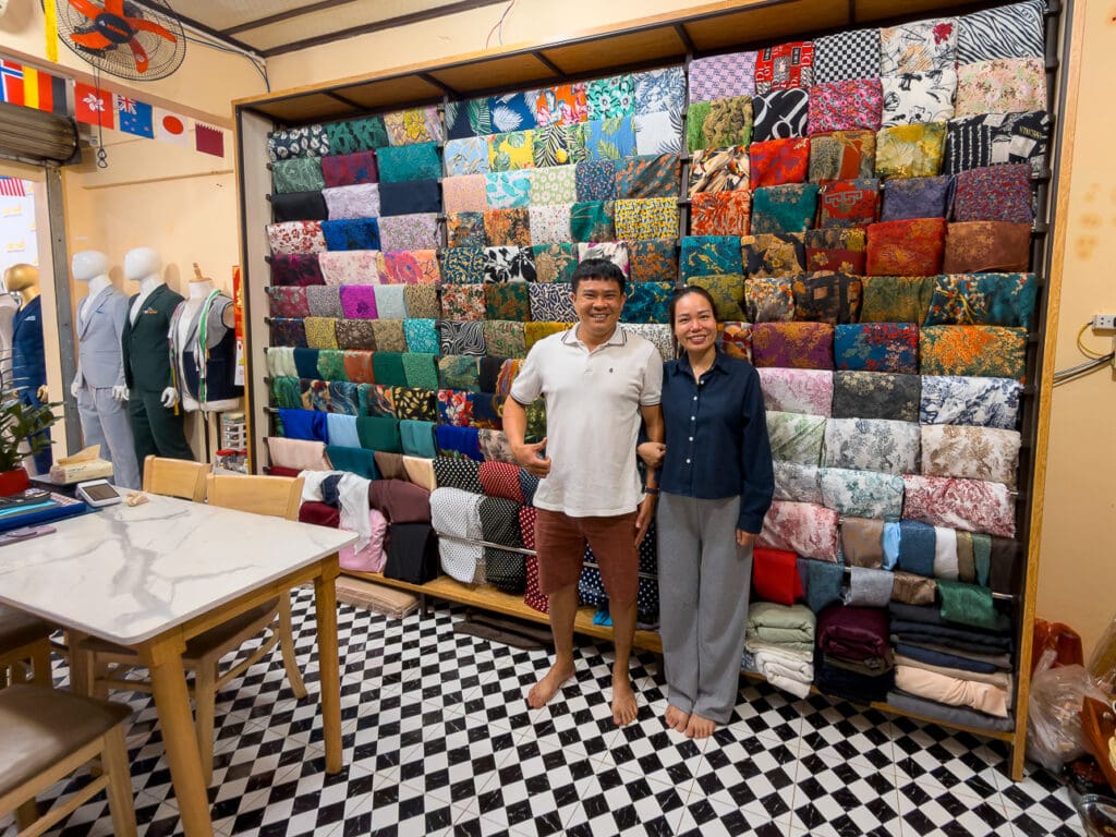Linh and her husband at Linh tailor in Hoi An, by the wall of fabric swatches
