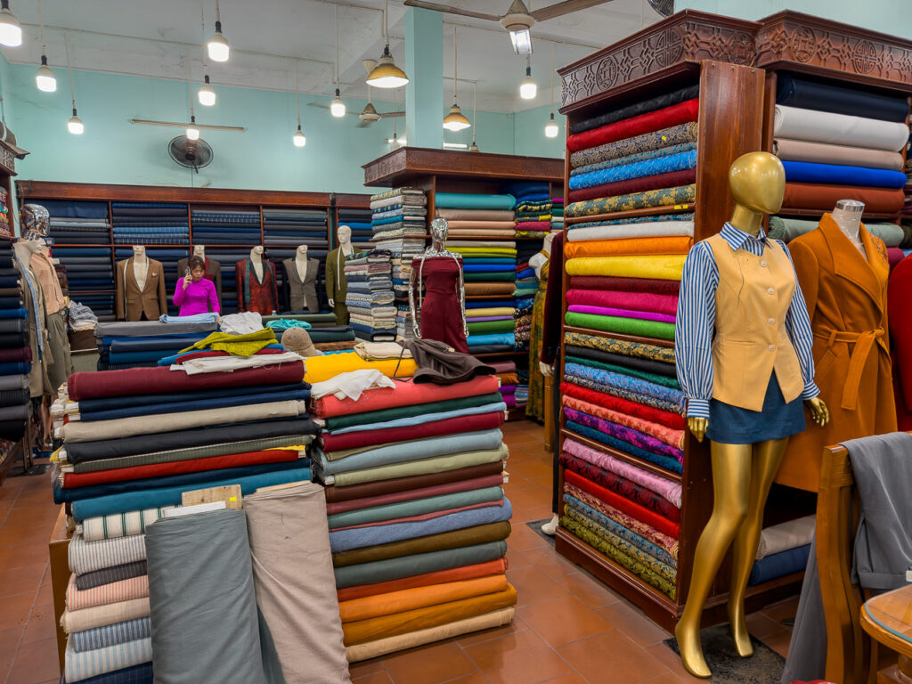 Tall shelves of folded fabric beside a styled mannequin at Pink Lotus Tailor, Hoi An