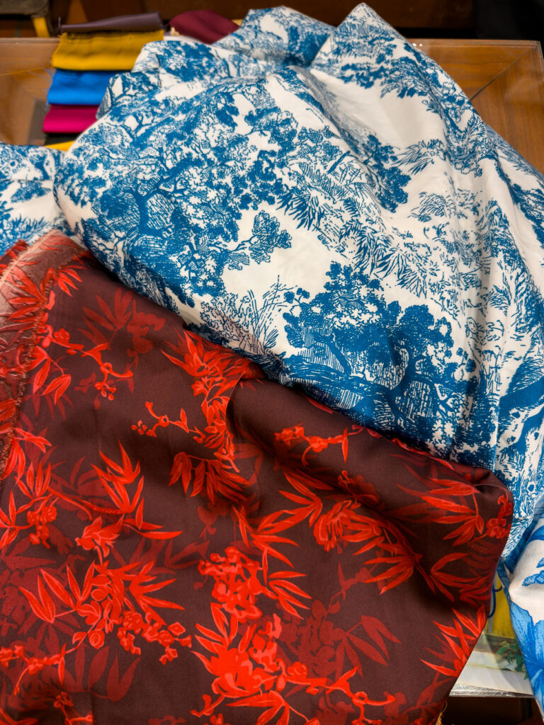 Blue and white toile fabric beside a red floral print at Blue Lantern tailor in Hoi An