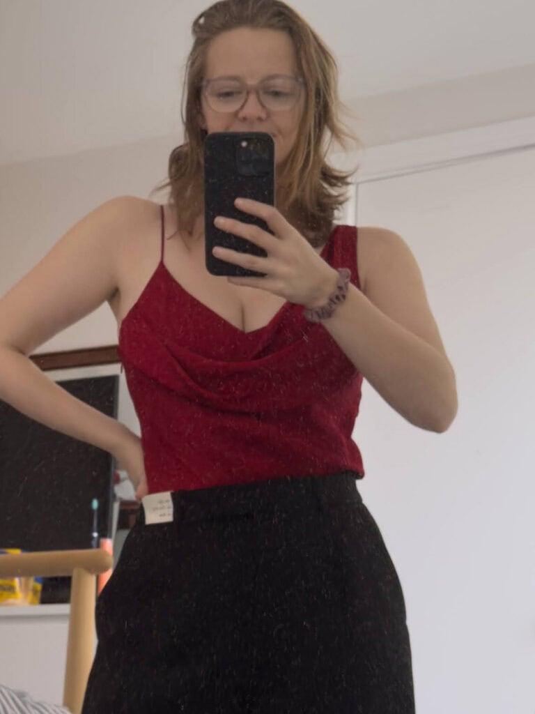 Alexx wearing a deep red satin cowl neck dress tucked into black trousers, the style used as a copy reference