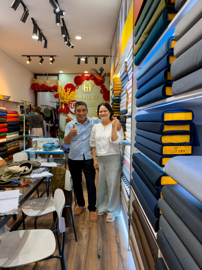 Heidi and her husband at Heritage tailor in Hoi An, by the blue fabric shelves