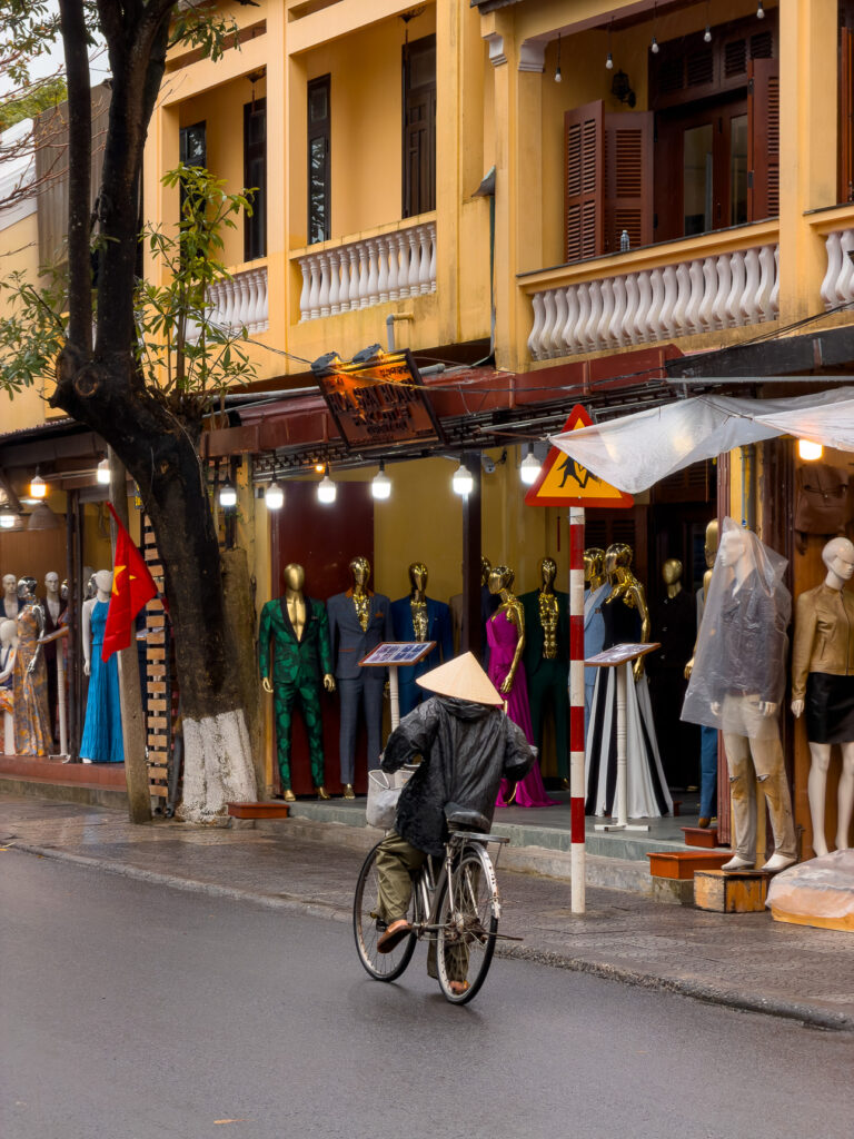 Yellow shopfronts and a cyclist in a conical hat on a tailoring street in Hoi An