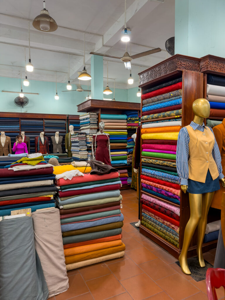Stacks of colourful fabric bolts and a dressed mannequin inside Pink Lotus Tailor in Hoi An