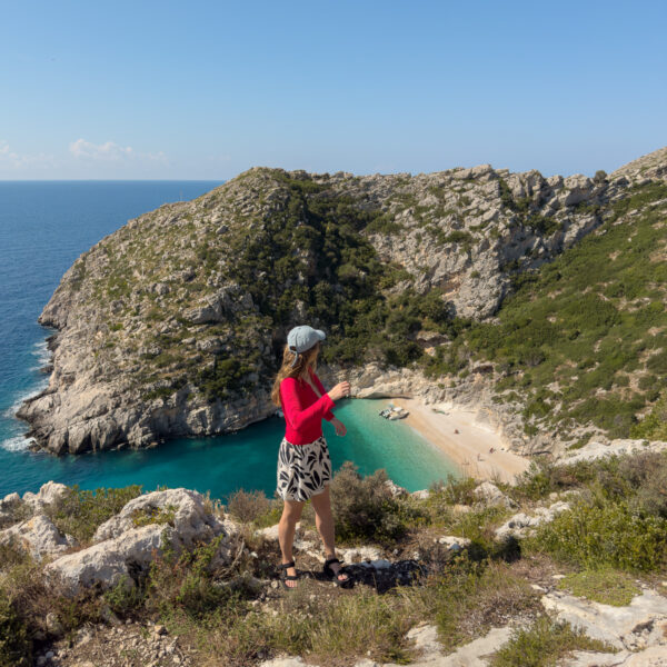 A solo female traveller in Albania enjoying the view over a secluded turquoise beach cove on a Riviera boat trip, showing off-the-beaten-path discoveries