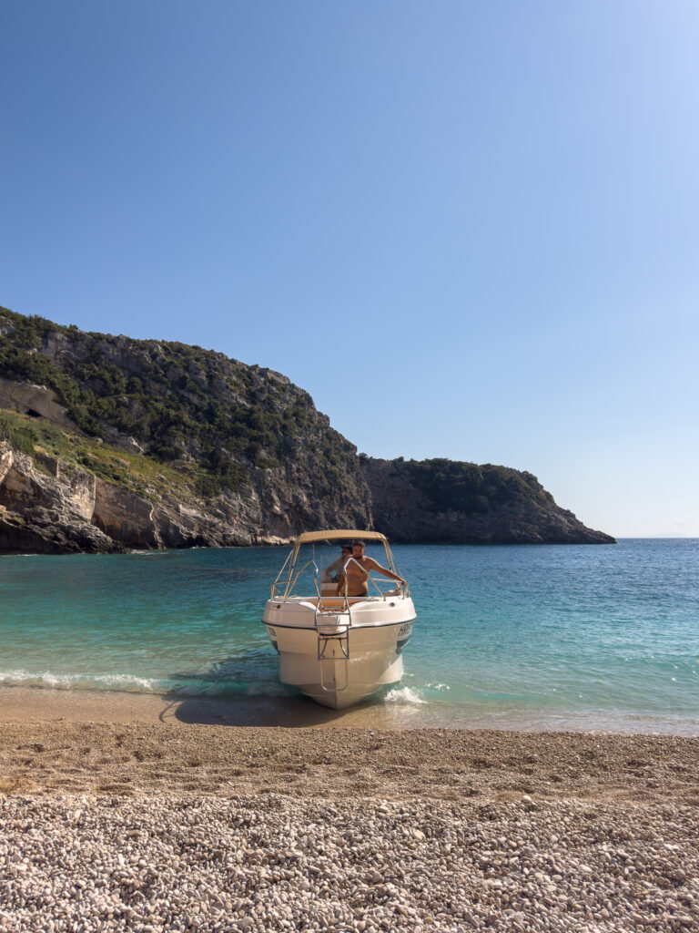 Staying safe in Albania: peaceful scene of single boat resting on transparent waters of Grama Bay beach between protective rocky headlands.