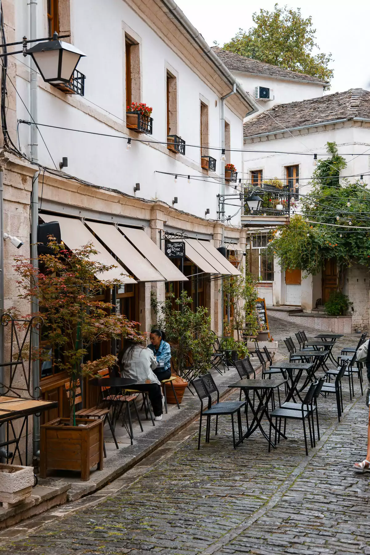 Morning light illuminates an empty cafe courtyard, weathered stone walls and climbing vines adorning traditional Gjirokaster architecture