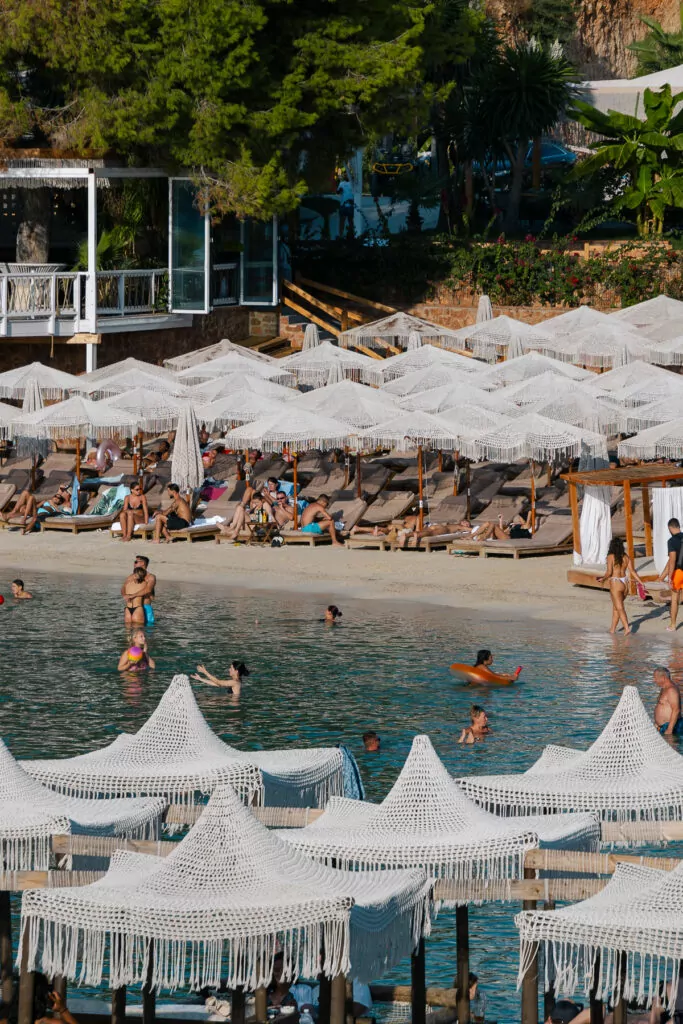 Summer beachgoers in Ksamil, Albania, with white umbrellas