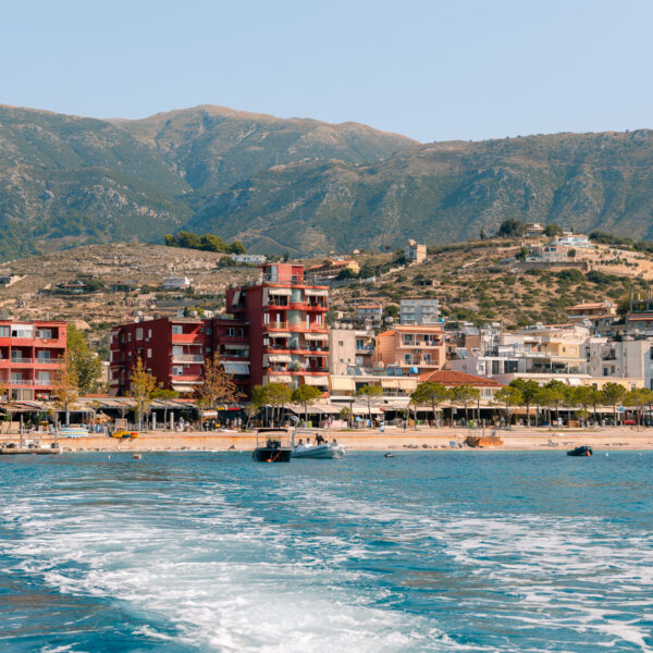 A view of colourful beachfront buildings in Himare, Albania, seen from a boat on bright blue waters