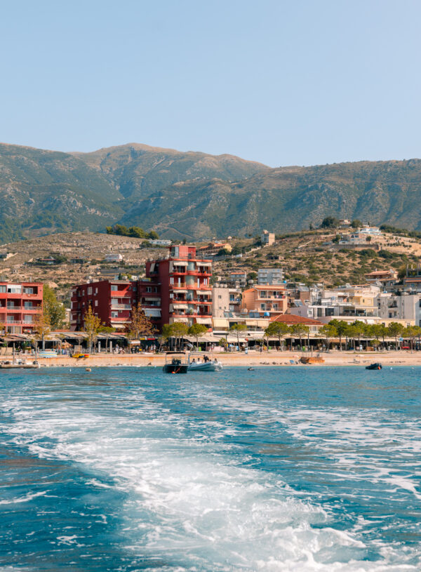 A view of colourful beachfront buildings in Himare, Albania, seen from a boat on bright blue waters