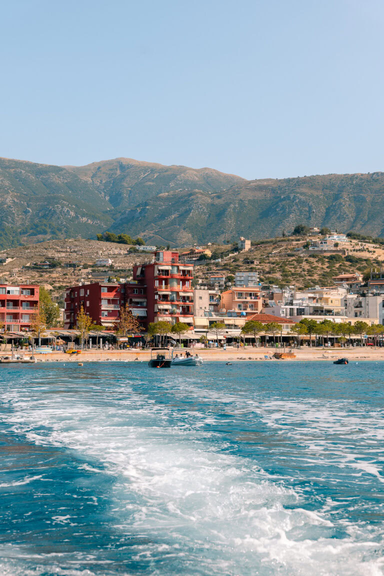 A view of colourful beachfront buildings in Himare, Albania, seen from a boat on bright blue waters
