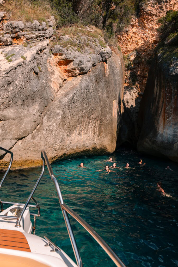 Solo travel in Albania means joining boat tours like this one, where swimmers enjoy deep turquoise waters in a hidden cove beneath towering limestone cliffs.