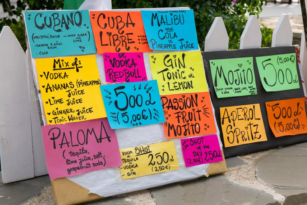 A handwritten board displays beach club drinks prices in the Albanian Riviera