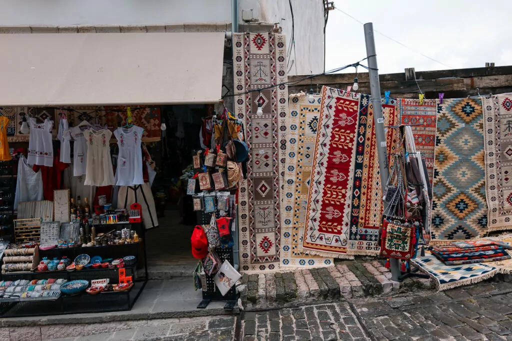 Traditional Albanian carpets burst with red and earth-toned patterns at Gjirokastër Bazaar where solo travellers browse textiles hanging from stone walls.