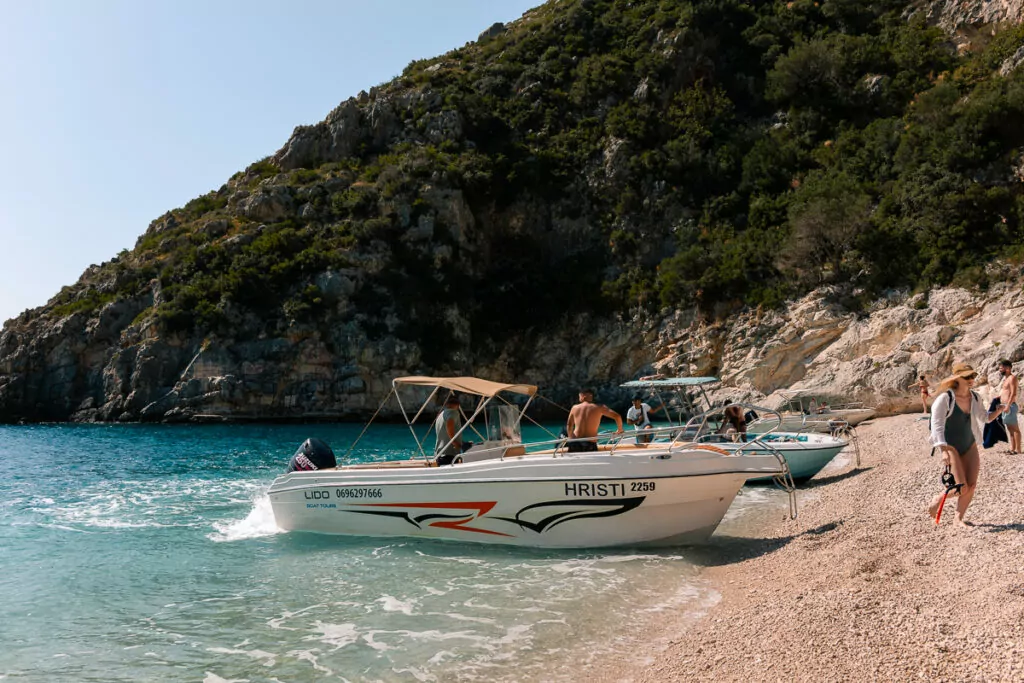 Boat tour in Albania explores the Riviera's pristine shore, where speedboats rest on white pebbles beside crystal-clear waters.