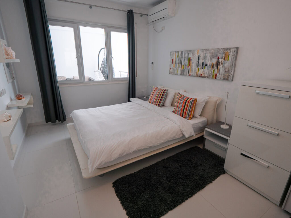 comfortable accommodation with white bedroom featuring queen bed, black rug, and abstract wall art