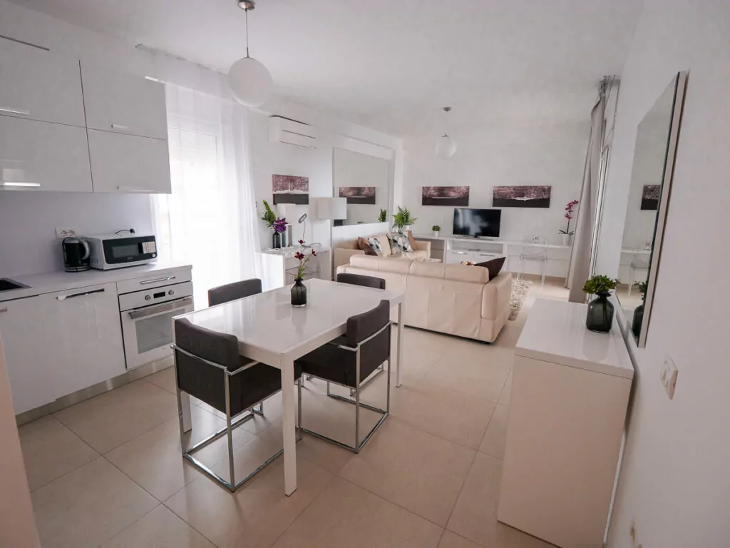 bright, open-plan apartment with white kitchen flowing into dining area and cream living room with modern furnishings