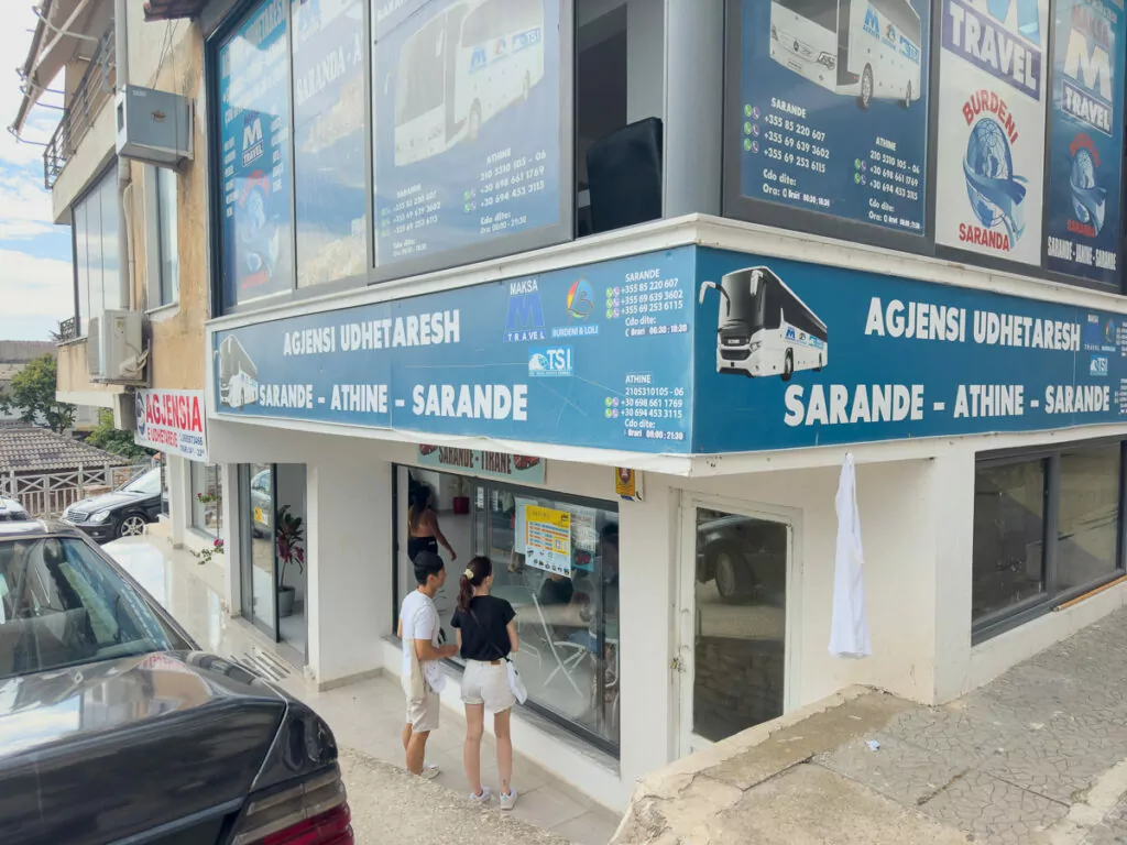 A travel agency storefront in Sarandë displays colourful posters advertising local excursions, typical of tourism services in Albania's beach towns.