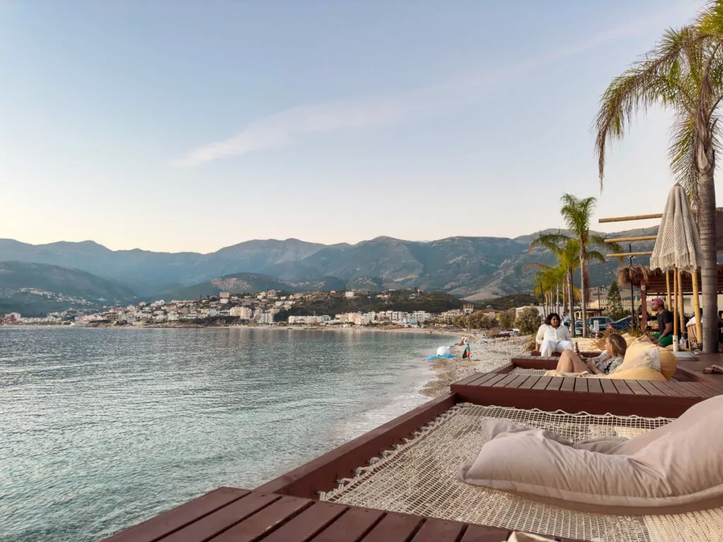 Beachfront loungers and palm trees create a relaxed setting along Albania's coastline with mountain views