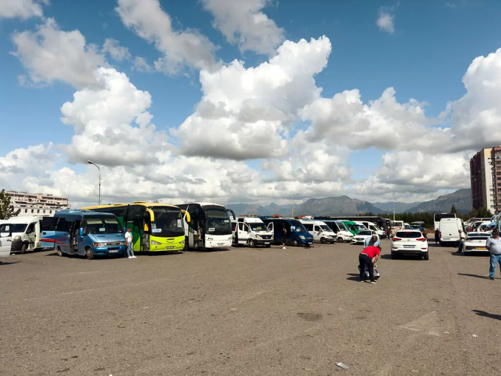 Albania solo travel guide shows modern bus station with colourful coaches lined up against mountain backdrop.